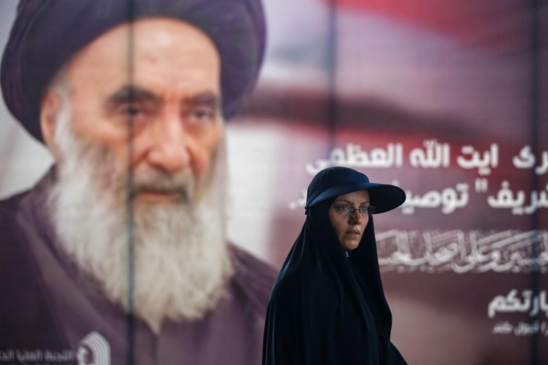 A woman stands next to a billboard bearing a portrait of Iraq's top Shiite Muslim cleric Grand Ayatollah Ali al-Sistani. (File/AFP)