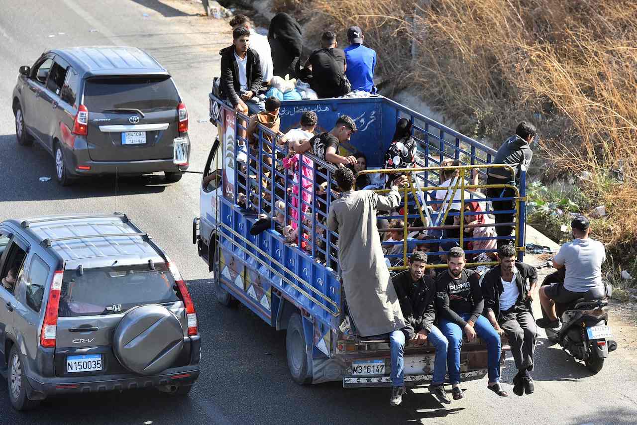 People sit with their belongings in the back of a truck as they arrive in the coastal town of Naameh, south of Lebanon's capital Beirut on September 24, 2024, as they flee their homes in southern Lebanon. (AFP)