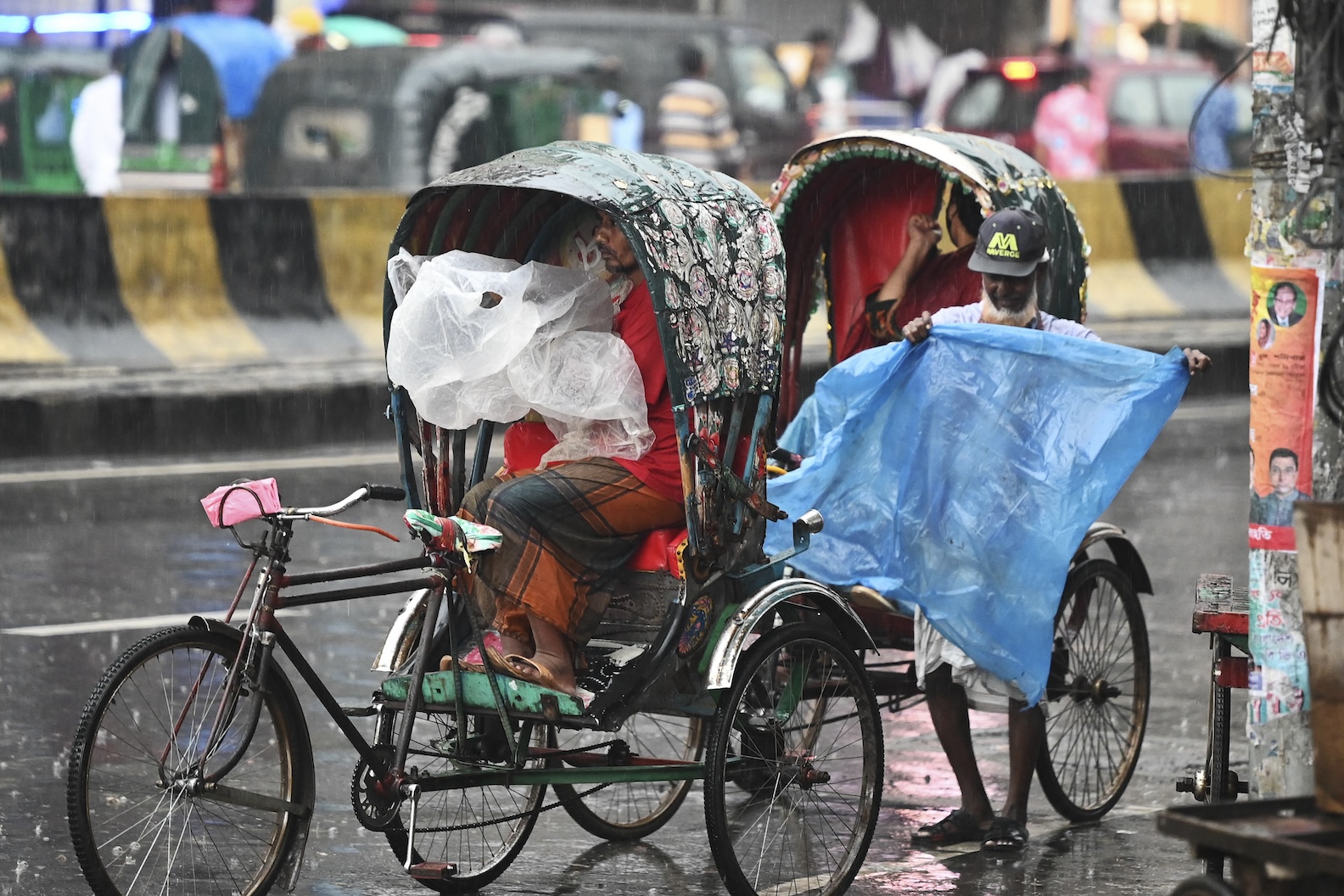 Rickshaw pullers shelter from the rain with a plastic sheet along a street in Dhaka on June 9, 2023. (AFP)