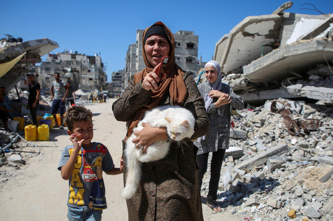 A Palestinian woman holds a cat as she walks pas the rubble of houses destroyed in the Israel’s military offensive in Khan Younis on Sept. 26, 2024. (Reuters)