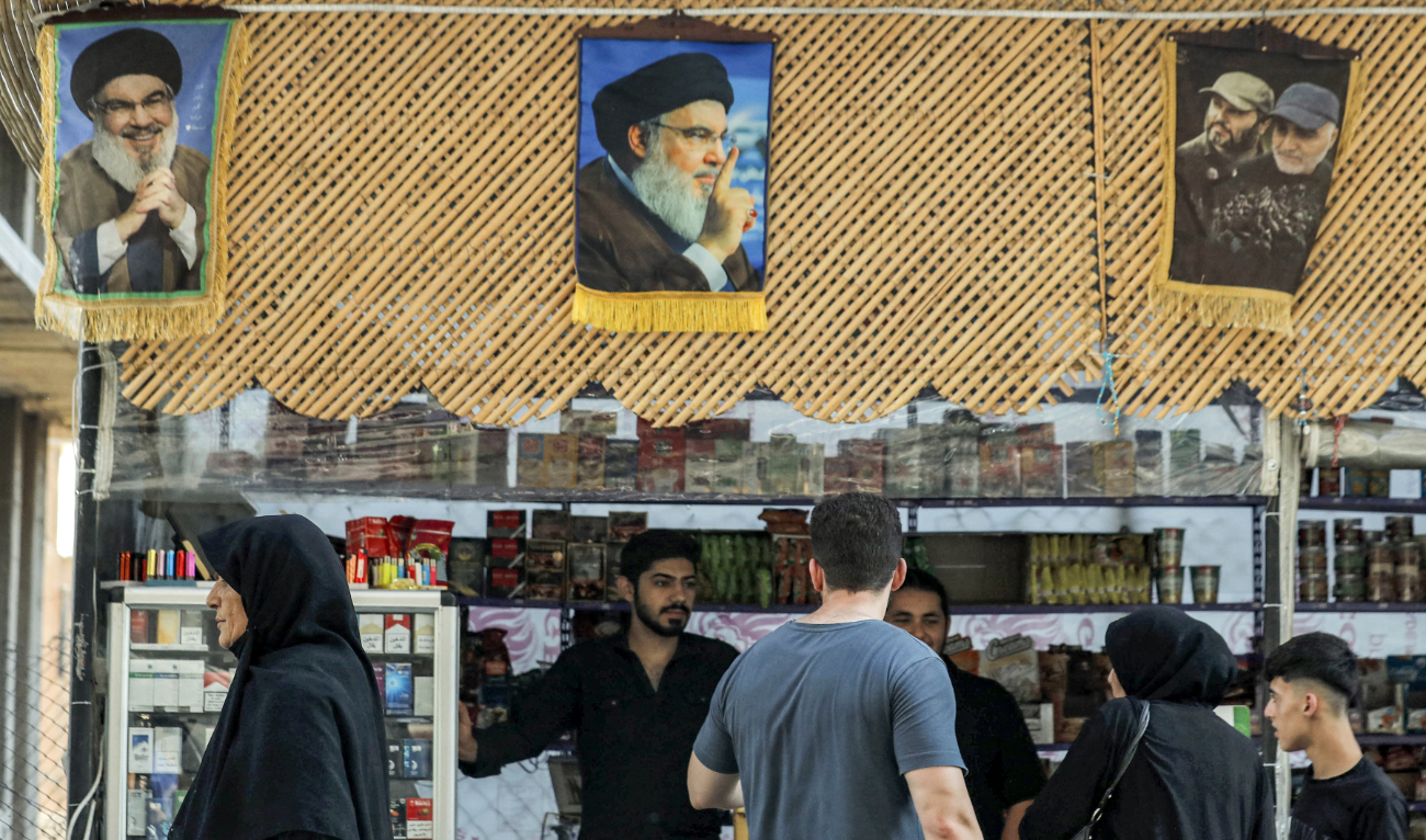 Pictures of Hassan Nasrallah (L and C) hang above a stall as people shop in Damascus' Sayyida Zeinab district on September 29, 2024. (AFP/File)