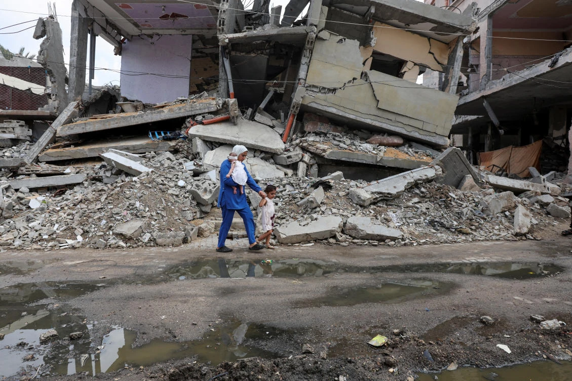 A displaced Palestinian mother walks past the rubble of a house destroyed in an Israeli strike as she returns to her shelter with her daughters after they got vaccinated against polio. (REUTERS)