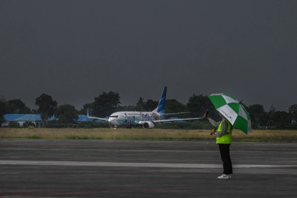 A girl with umbrella takes selfies as a passenger plane of Garuda Indonesia airline takes off from the runway at the Sultan Iskandar Muda International Airport in Blang Bintang, Aceh province on July 10, 2024. (AFP)