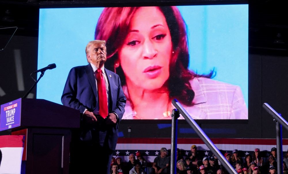 Donald Trump looks on as Kamala Harris’ face appears on a screen, during a rally in Detroit, Michigan, Oct. 18, 2024. (Reuters)
