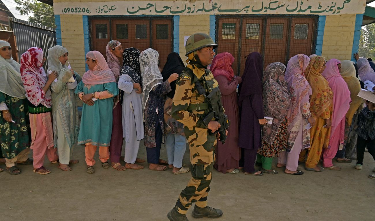 An Indian security personnel stands guard as voters queue up to cast their ballots at a polling station during the third and final phase of voting for local assembly elections, in Bandipora on October 1, 2024. (AFP)