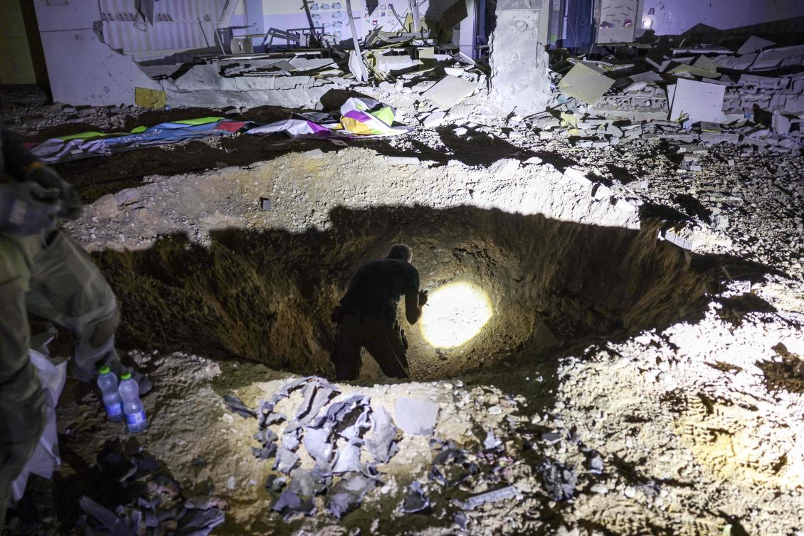 Members of Israel’s Home Front Command and police forces inspect a crater left by an exploded projectile at a heavily-damaged school building in Israel’s southern city of Gedera on Oct. 1, 2024, after Iran launched a barrage of missiles at Israel. (AFP)