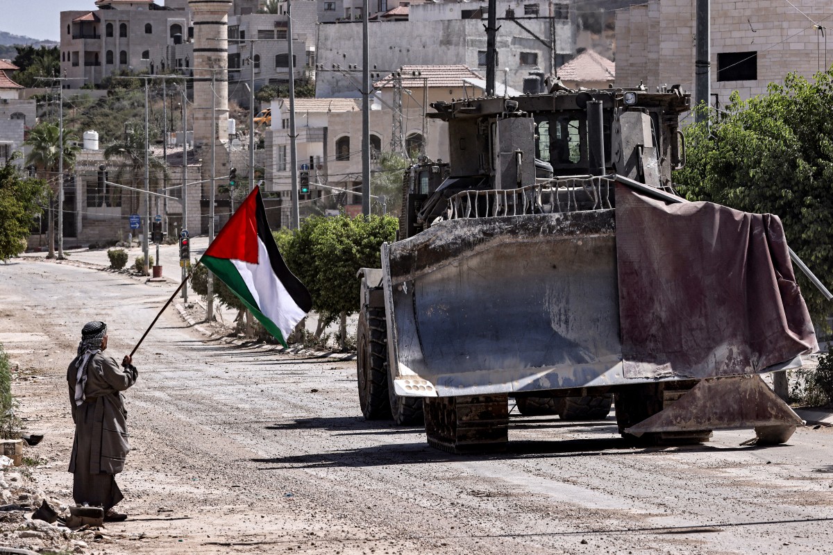 A Palestinian activist holding a national flag stands by as an Israeli army bulldozer moves during an ongoing raid on the Tulkarm camp for Palestinian refugees in the north of the occupied West Bank on September 12, 2024.(AFP)