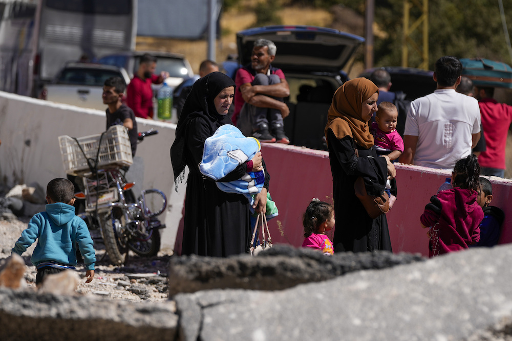 People carry their luggage as they cross into Syria on foot, through a crater caused by Israeli airstrikes aiming to block Beirut-Damascus highway at the Masnaa crossing, in the eastern Bekaa Valley, Lebanon on Oct. 5. (AP)