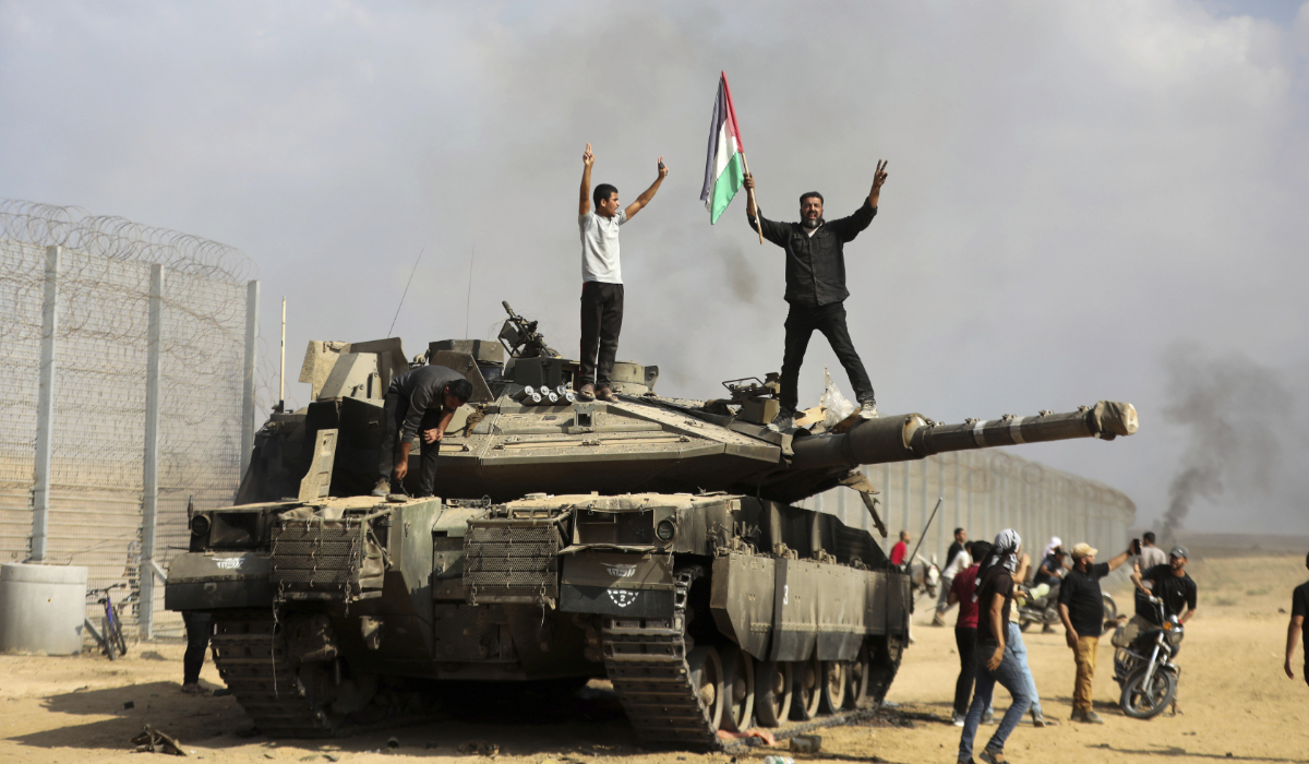 Palestinians wave their national flag and celebrate by a destroyed Israeli tank at the southern Gaza Strip fence east of Khan Younis on Saturday, Oct. 7, 2023. (AP)