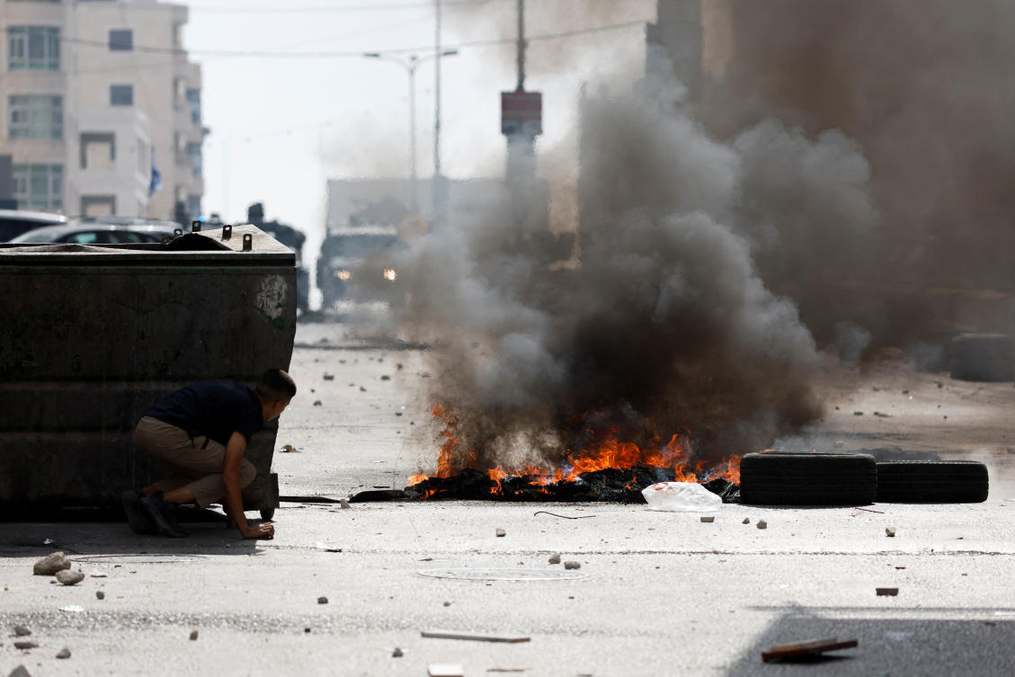 A Palestinian boy takes cover near burning tires during an Israeli raid in Qalandya, in the Israeli-occupied West Bank. (Reuters)