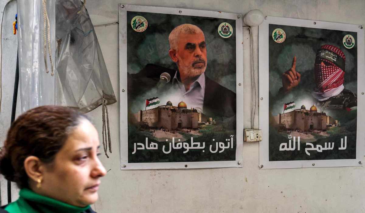 A woman walks past posters depicting Yahya Sinwar (L), the head of the political wing of the Palestinian Hamas movement in the Gaza Strip, and Abu Obeida (R), the masked spokesman of the Qassam Brigades (Hamas' armed wing), plastered on a wall in the Burj Al-Barajneh camp for Palestinian refugees in Beirut's southern suburb on February 5, 2024. (AFP)
