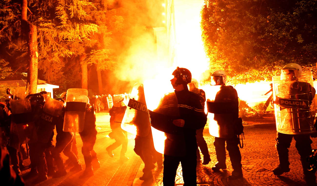 Riot police officers stand in a street as molotov cocktails explode outside the government building, thrown by opposition protesters who demand the resignation of the government and the release of opposition MP Ervin Salianji, in Tirana, on October 7, 2024. (AFP)