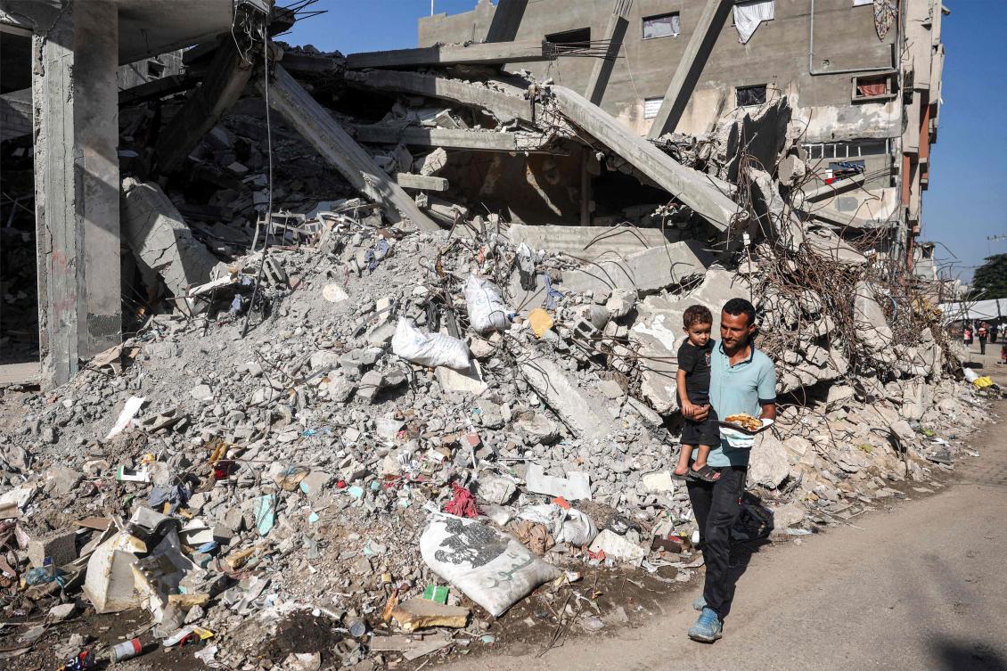 A man carries a child while walking past a collapsed building in the Bureij camp for Palestinian refugees in the central Gaza Strip on October 9, 2024. (AFP)