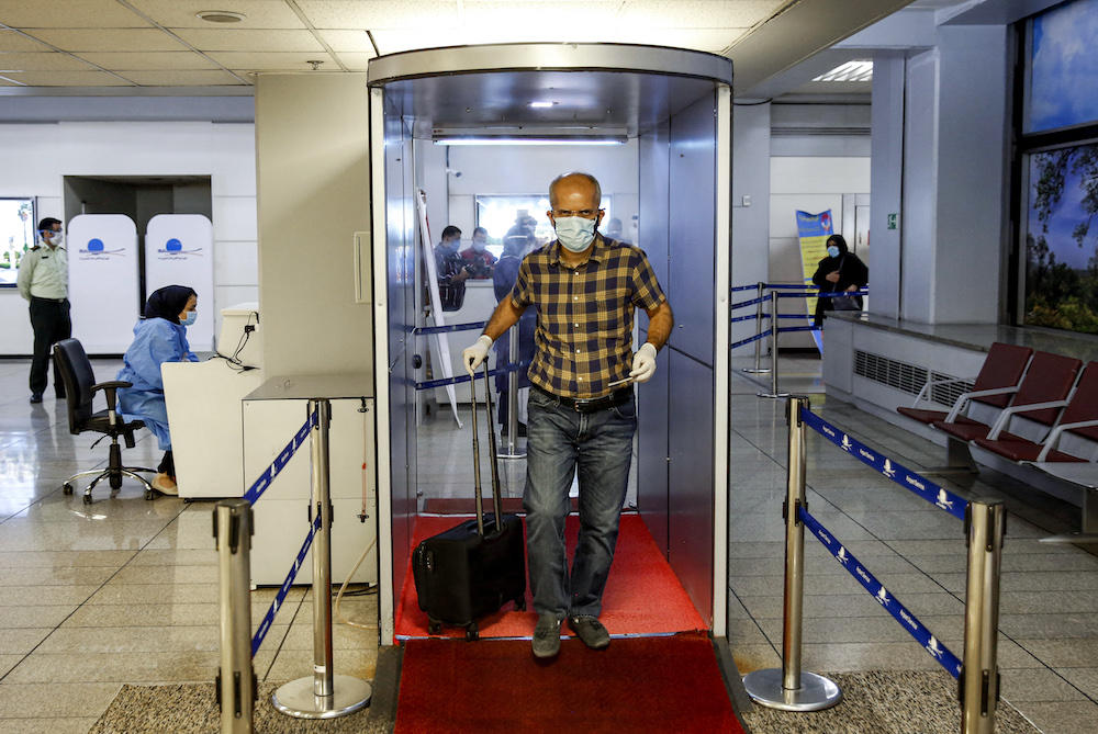 Above, an incoming passenger crosses with his luggage through a disinfection tunnel upon arriving at Tehran’s Imam Khomeini International Airport on July 17, 2020. (AFP file photo)