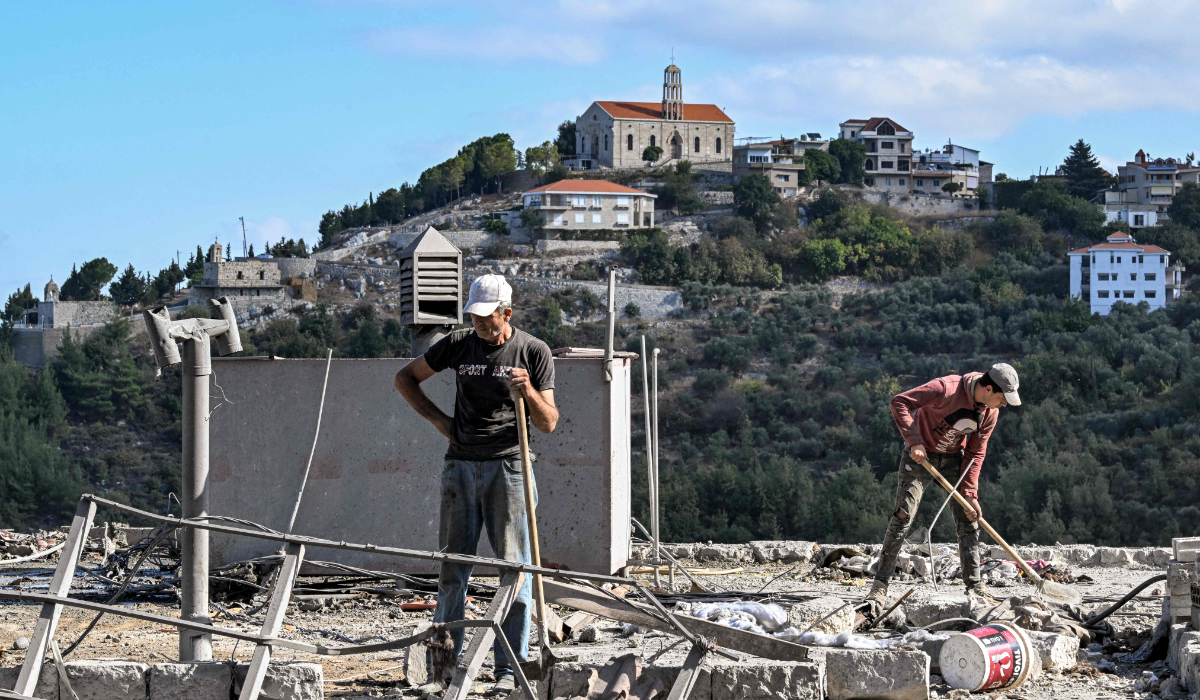 Men clear debris off the roof of a building by the site of a previous Israeli air strike on the village of Aito in northern Lebanon on October 15, 2024. (AFP)