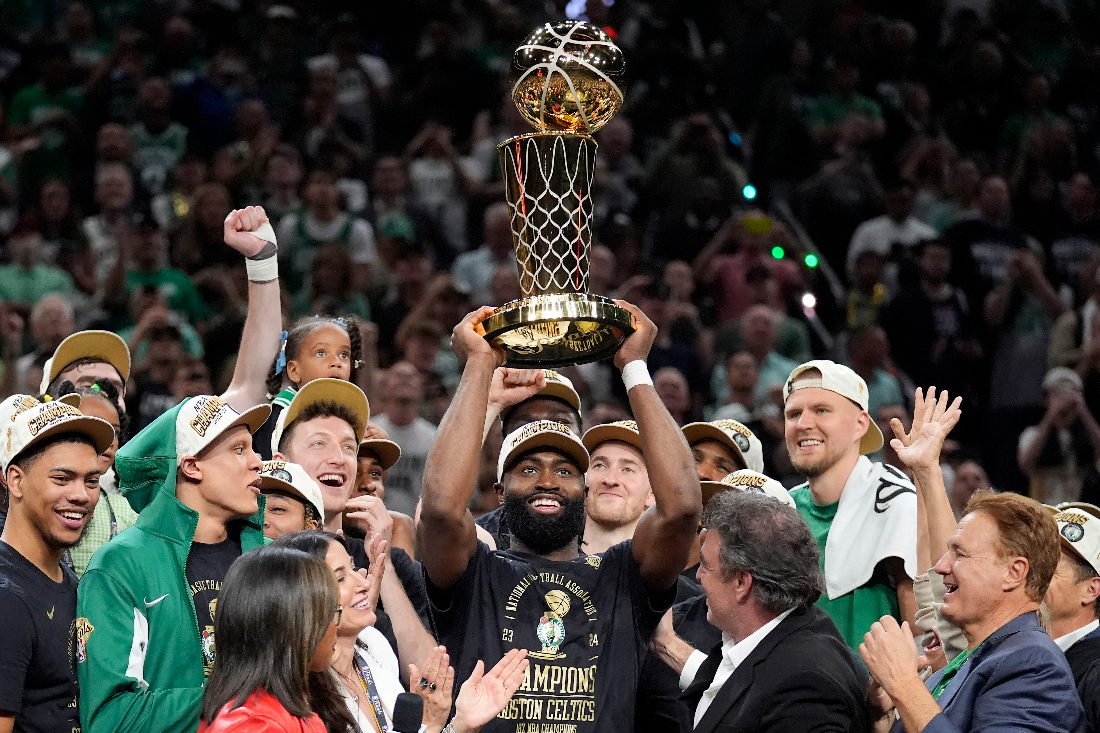 Boston Celtics guard Jaylen Brown, center, holds up the Larry O'Brien Championship Trophy as he celebrates with the team after they won the NBA basketball championship with a Game 5 victory over the Dallas Mavericks in Boston. (File/AP)