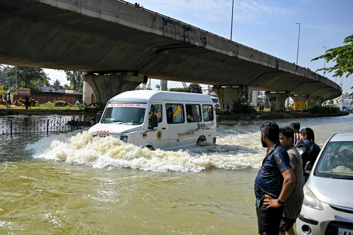 Locals watch as a State Disaster Response Force (SDRF) vehicle wades through a flooded street following heavy rainfall, in Bengaluru on October 22, 2024. (AFP)