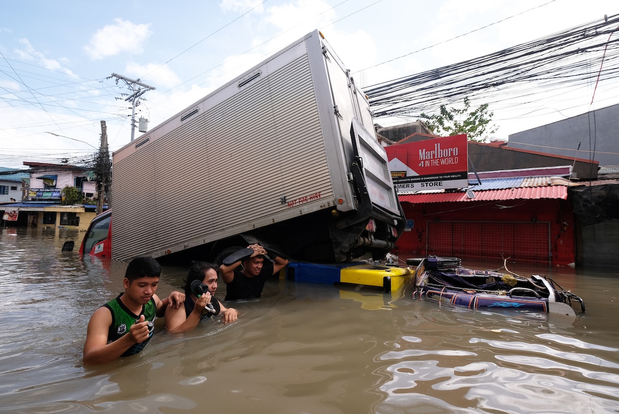 People wade through a flooded road brought about by Tropical Storm Trami in Naga, Camarines Sur, on Oct. 25, 2024. (AFP)