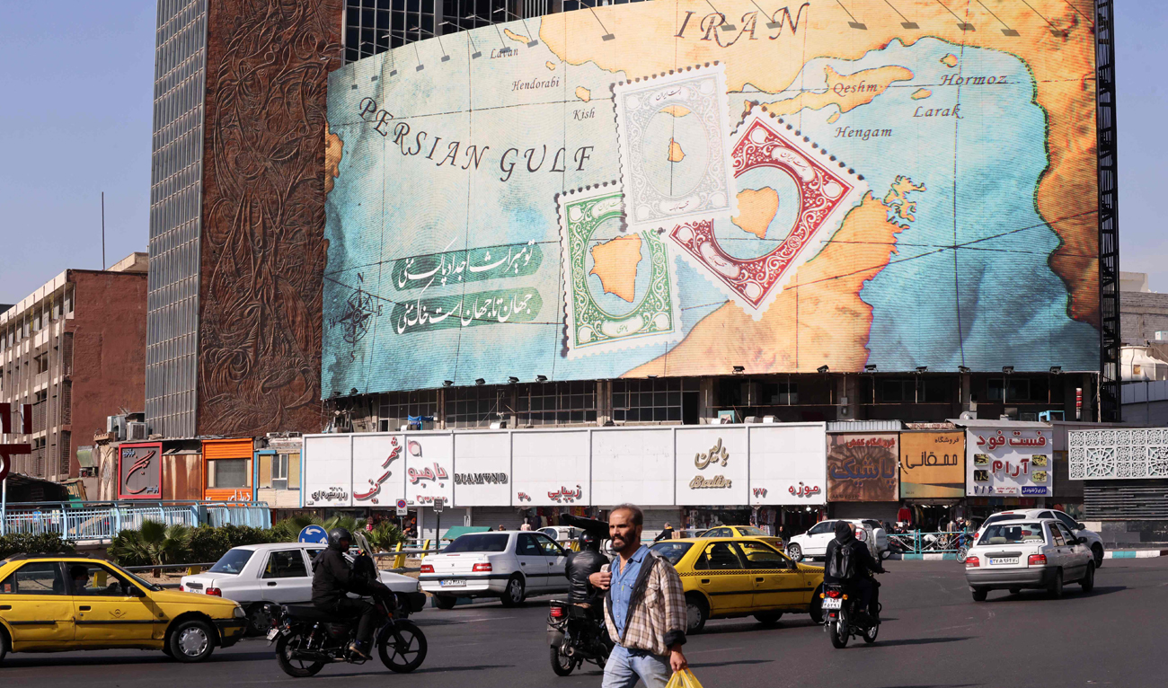 People walk and drive past a billboard covering the facade of a building on Vali-Asr square in Tehran on October 26, 2024. (AFP)