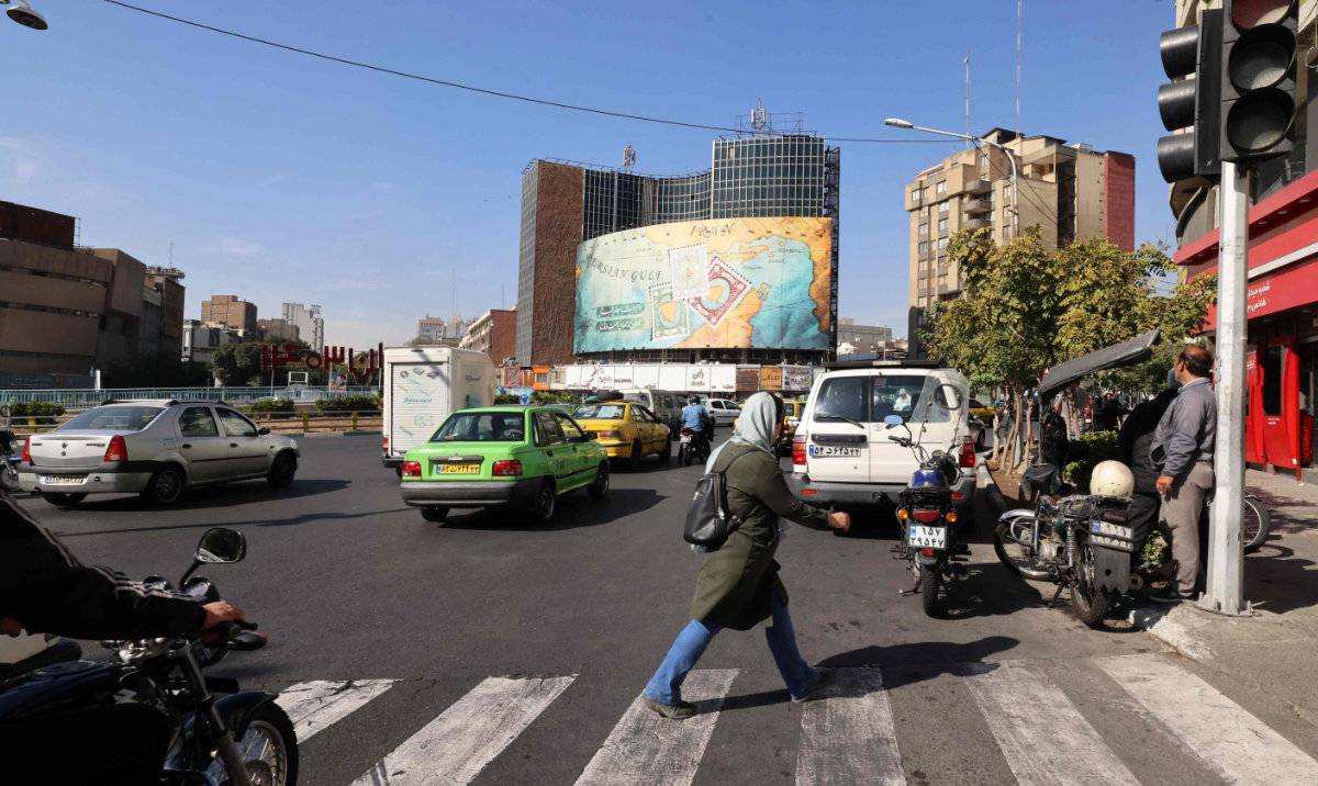 People walk and drive past a billboard covering the facade of a building on Vali-Asr square in Tehran on October 26, 2024. (AFP)