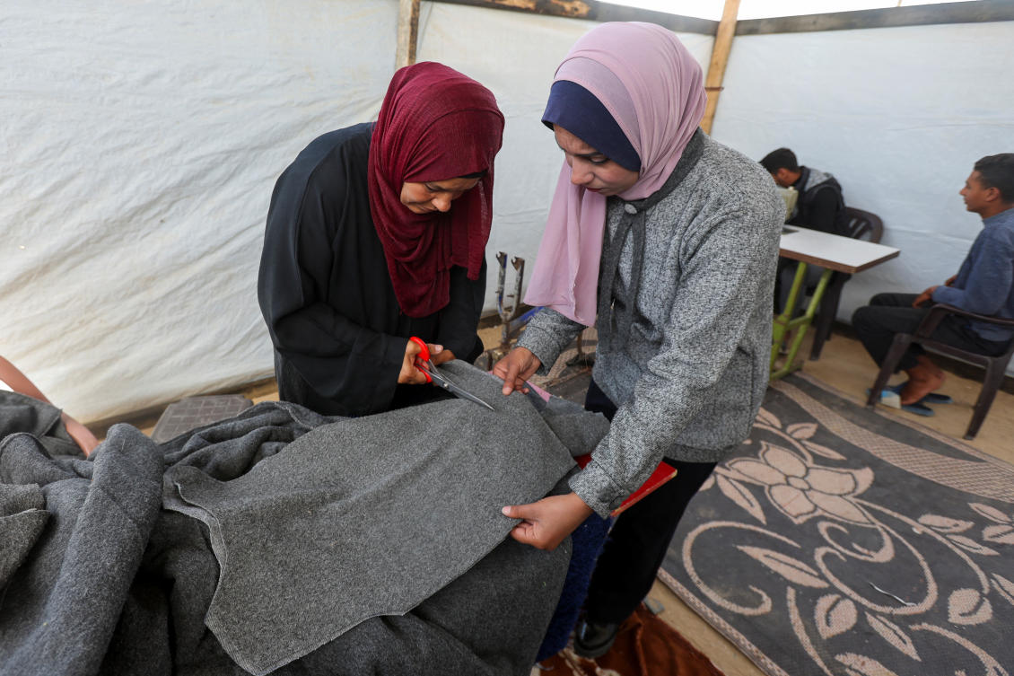 Palestinian Nidaa Attia (R) and another woman work to turn blankets into winter clothes for displaced people, amid clothing shortages, at a tent in Khan Younis in the southern Gaza Strip.(REUTERS)