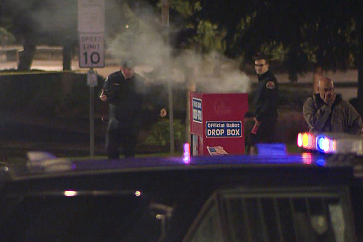 In this image made from a video provided by KGW8, authorities investigate smoke pouring out of a ballot box on MOct. 28, 2024, in Vancouver, Washington. (KGW8 via AP)