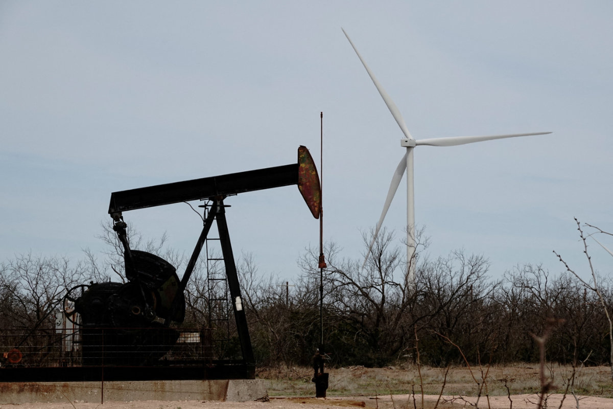 A pump jack drills oil crude from the Yates Oilfield in West Texas's Permian Basin, as a 1.5MW GE wind turbine from the Desert Sky Wind Farm is seen in the distance, near Iran, Texas, on March 17, 2023. (REUTERS/File Photo)