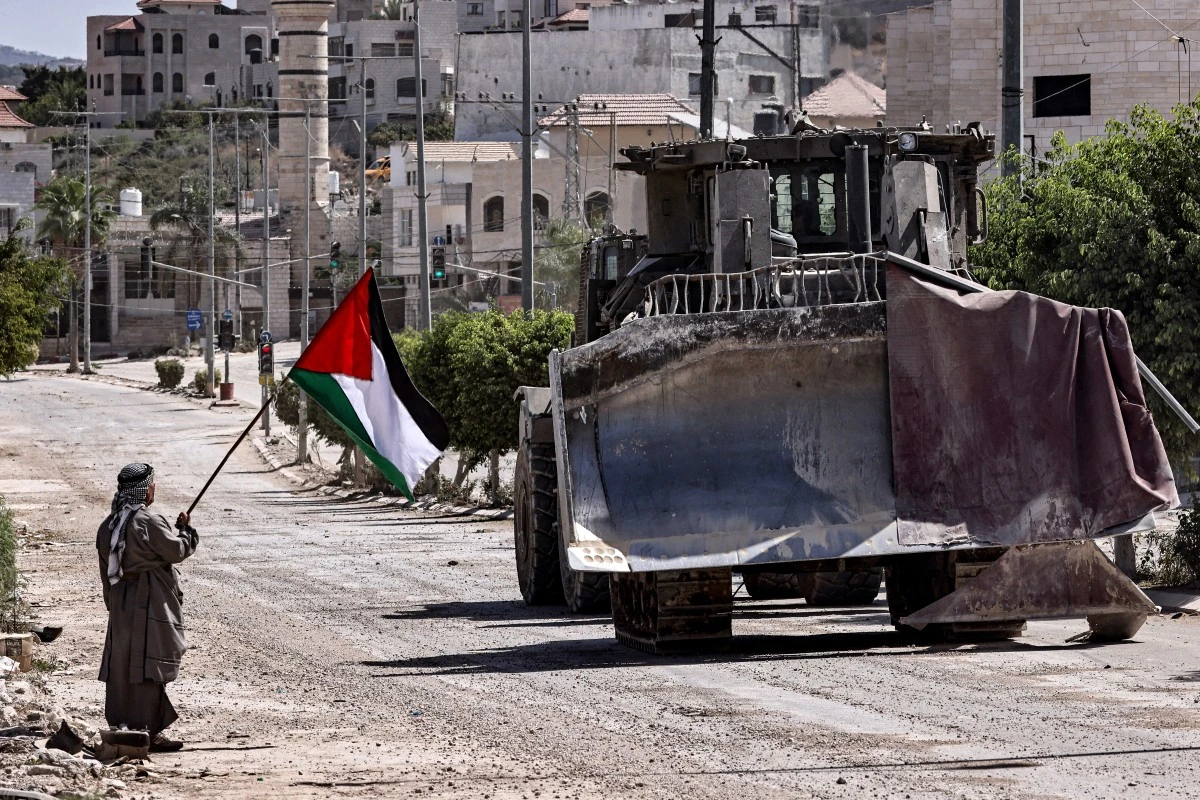 A Palestinian activist holding a national flag stands by as an Israeli army bulldozer moves during an ongoing raid on the Tulkarm camp for Palestinian refugees in the north of the occupied West Bank on September 12, 2024.(AFP)