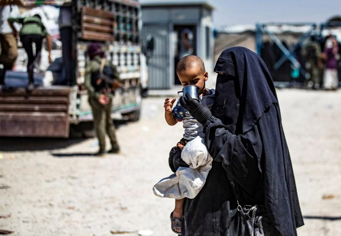A Syrian woman helps a child to drink as she waits with family members inside the Kurdish-run al-Hol camp, which holds relatives of suspected Islamic State (IS) group fighters in the northeastern Hasakeh governorate, before being released from the camp to return home in the northern Raqqa region, on July 15, 2021. (File/AFP)