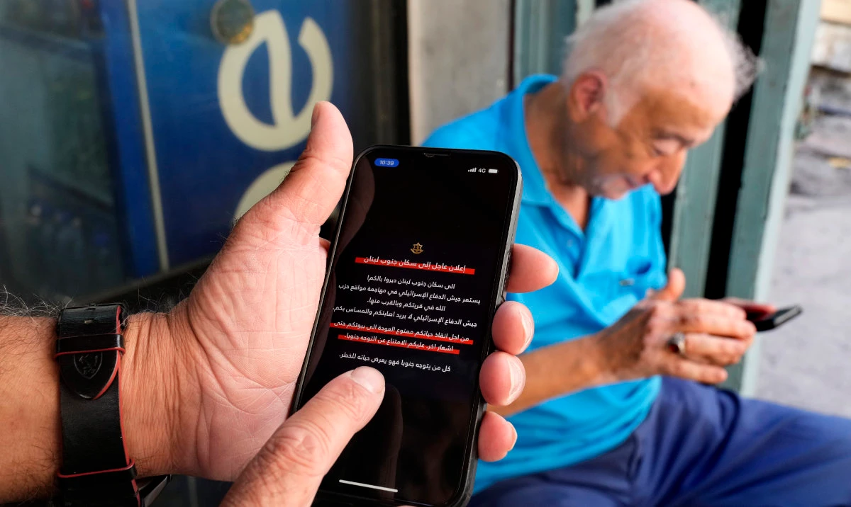 Men read mobile phone alerts telling residents of southern Lebanon not to return to their homes until further notice because of operations Israel says are targeting Hezbollah facilities in Beirut, Lebanon, Wednesday, Oct. 9, 2024. (AP)