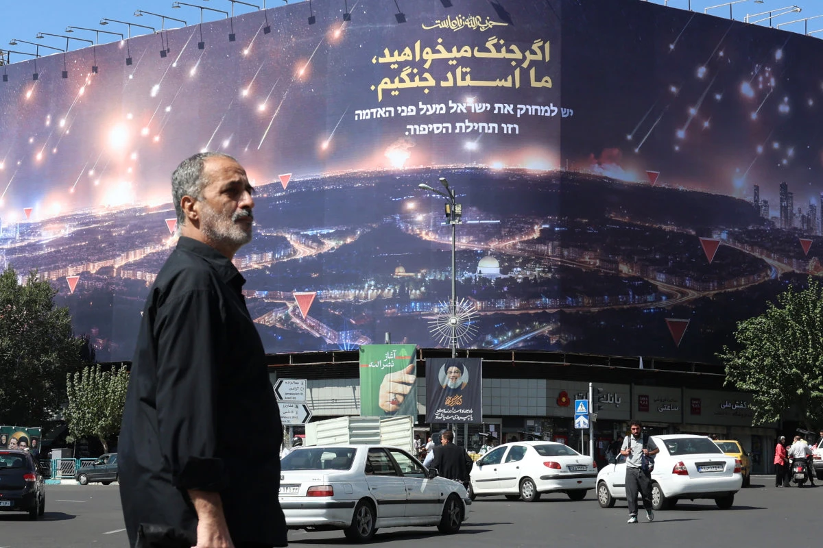 Iranians walk and drive past a billboard with an image depicting a missile attack over Israel and slogans reading in Farsi (top):" If you want war, we are masters of war" and in Hebrew: "Israel must be wiped from the face of the earth and this is the beginning of the story," in Tehran on October 3, 2024. (AFP)