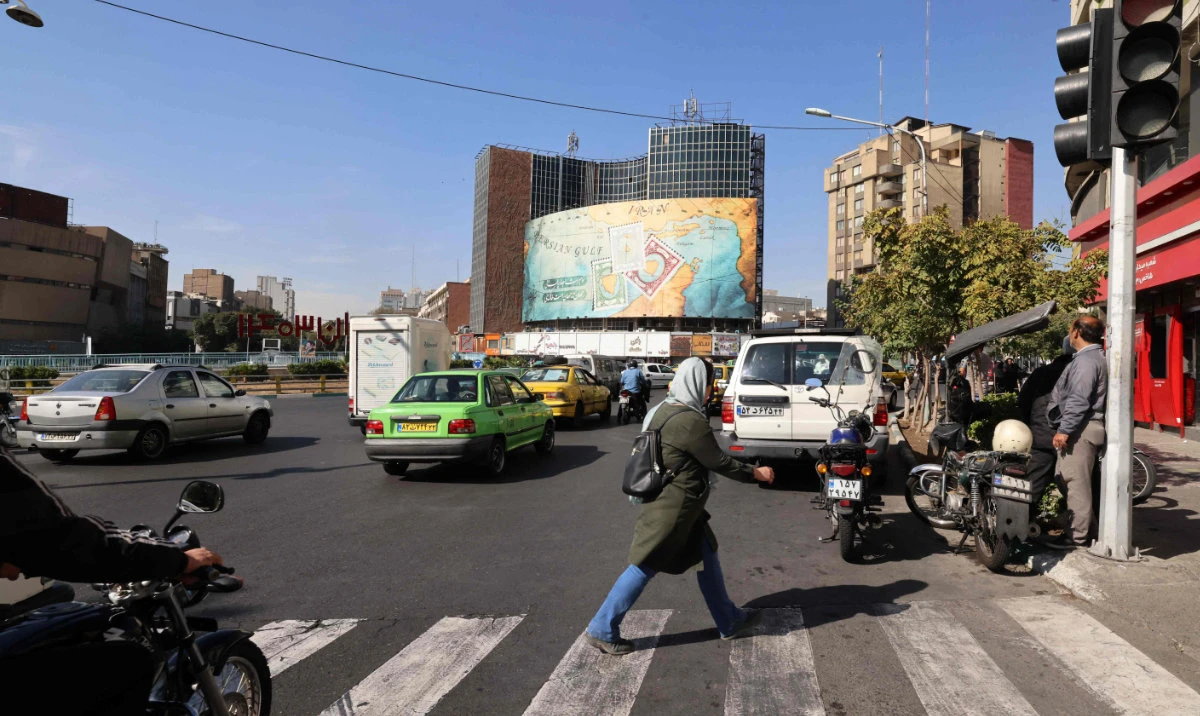 People walk and drive past a billboard covering the facade of a building on Vali-Asr square in Tehran on October 26, 2024. (AFP)