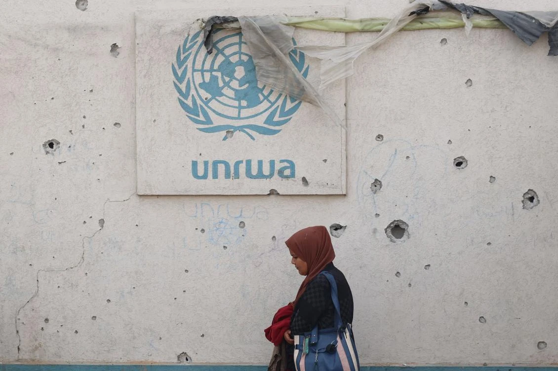 A Palestinian woman walks past a damaged wall bearing the UNRWA logo at a camp for internally displaced people in Rafah in the southern Gaza Strip. (AFP/File Photo)