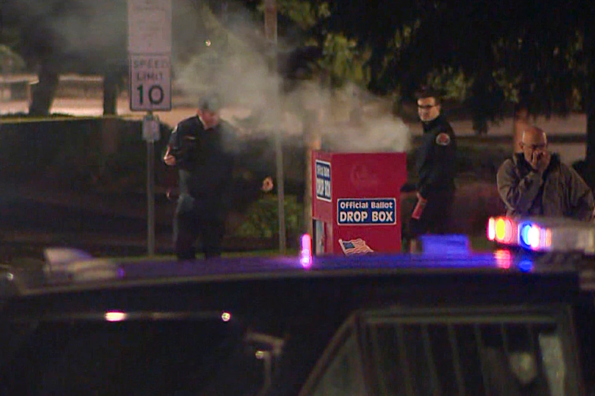 In this image made from a video provided by KGW8, authorities investigate smoke pouring out of a ballot box on MOct. 28, 2024, in Vancouver, Washington. (KGW8 via AP)