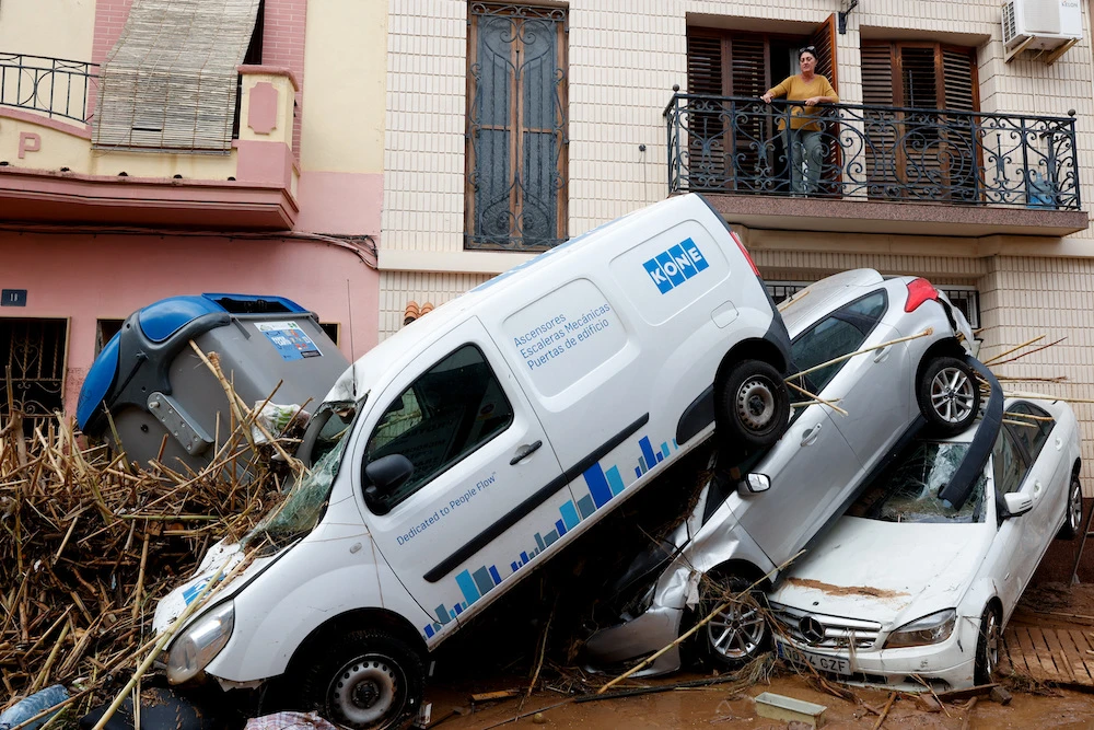 A woman looks from a balcony at piled up cars on a mud-covered street in the aftermath of torrential rains that caused flooding, in Paiporta, Spain, Oct. 31, 2024. (Reuters)