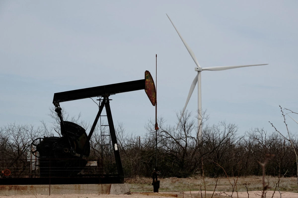 A pump jack drills oil crude from the Yates Oilfield in West Texas's Permian Basin, as a 1.5MW GE wind turbine from the Desert Sky Wind Farm is seen in the distance, near Iran, Texas, on March 17, 2023. (REUTERS/File Photo)