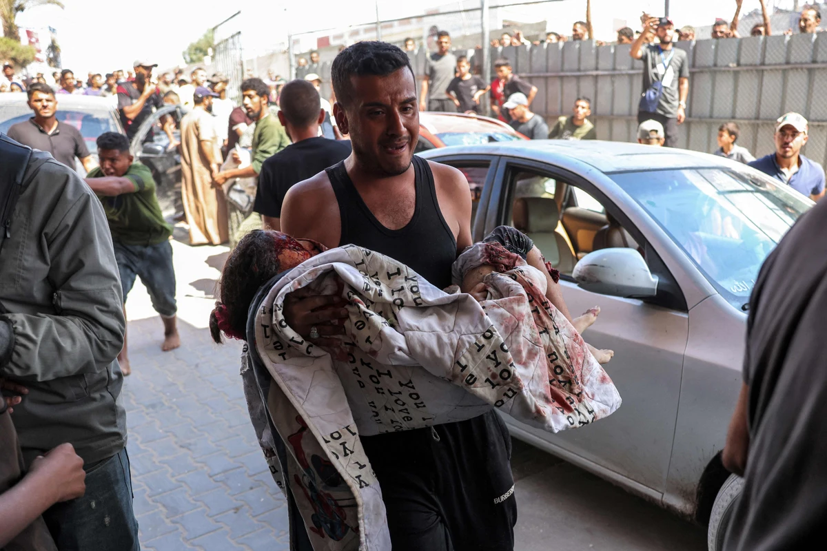 A man reacts while carrying a severely injured girl following Israeli bombardment on a displacement camp in Khan Yunis. (AFP)