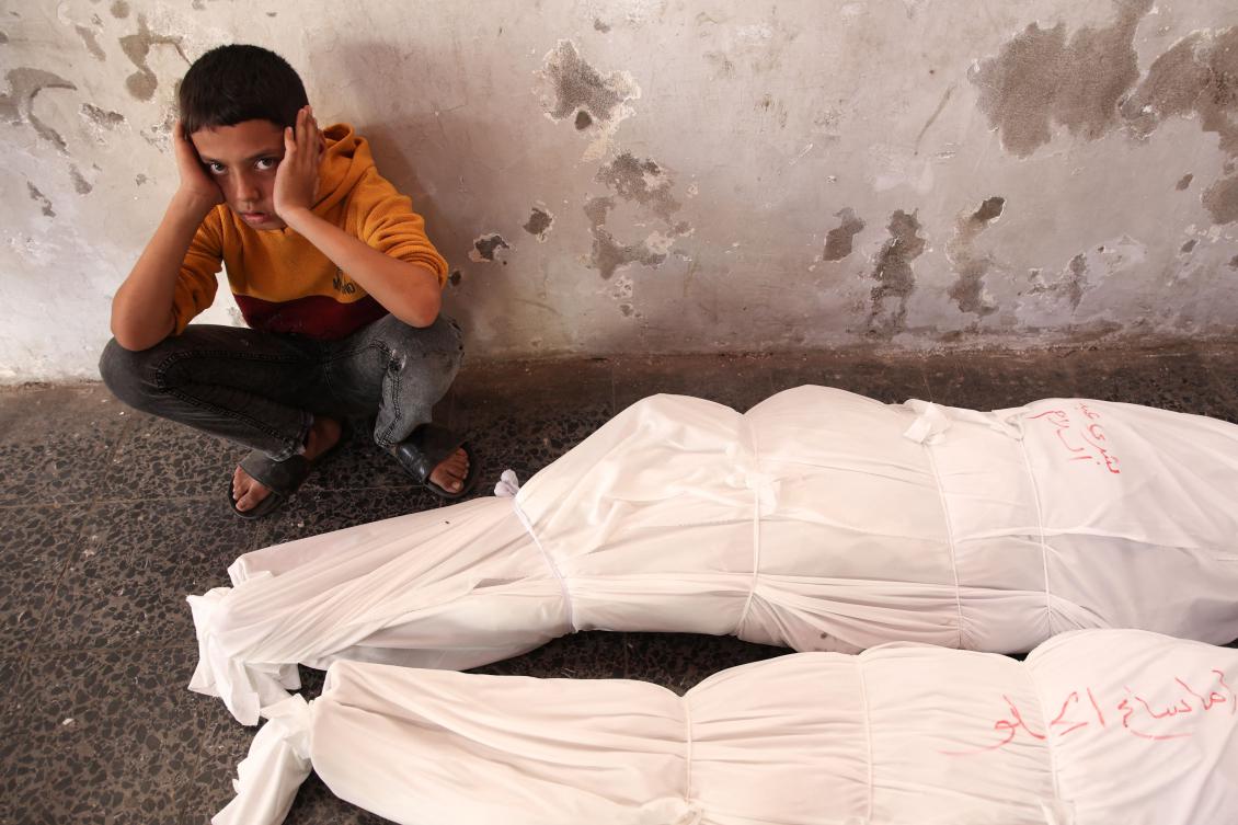 A Palestinian child sits next to the shrouded bodies of people killed in an Israeli strike. (AFP)