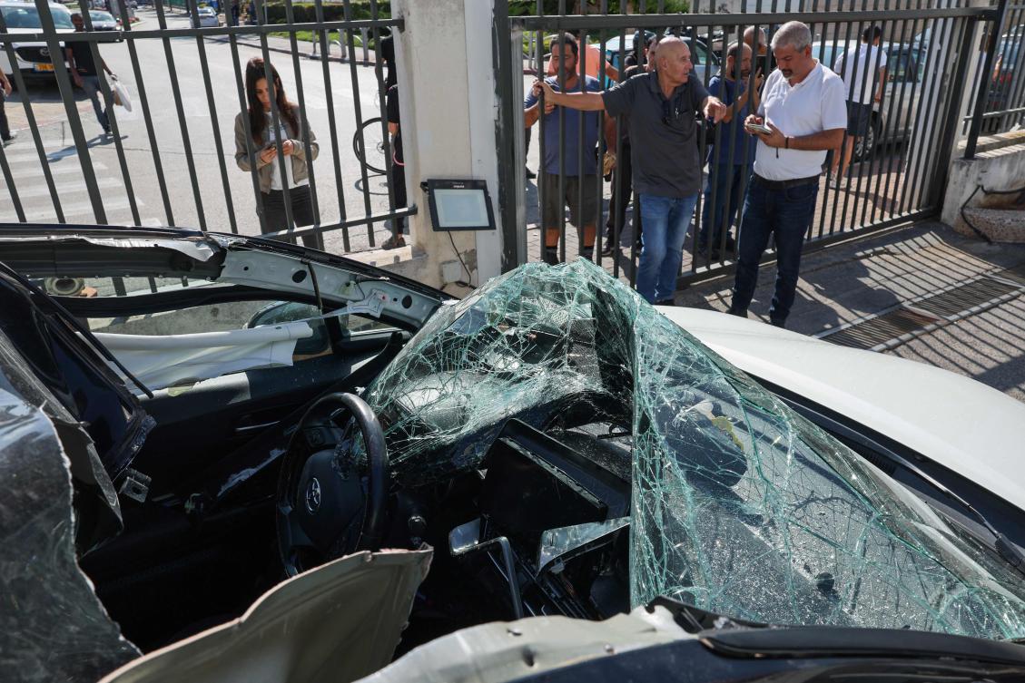 People look at a damaged car where an artillery shell fell before it was removed by Israeli police in Raanana near Tel Aviv on Nov. 6, 2024, following a reported barrage of rockets launched from Lebanon toward Israel. (AFP)