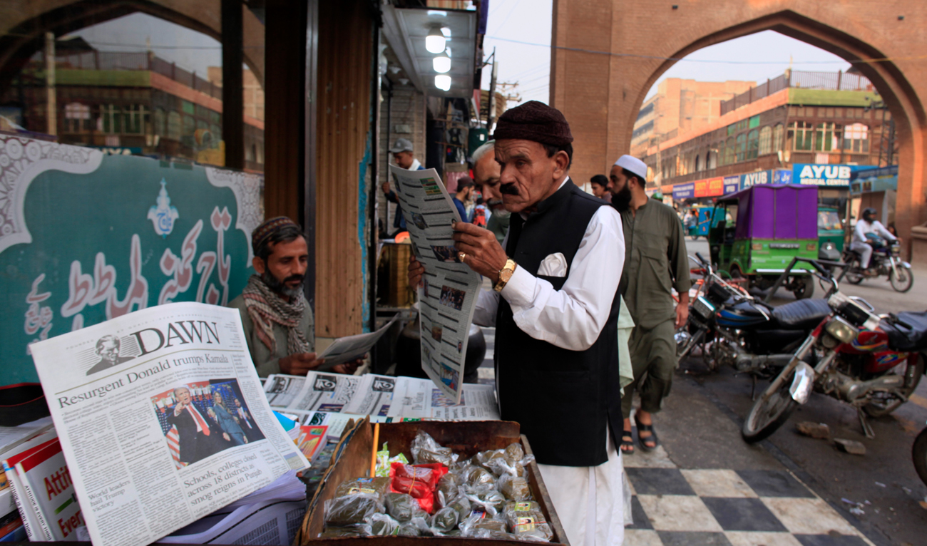 Pakistanis read morning newspapers which cover headline story about the results of US presidential elections, at a stall in Peshawar on November 7, 2024. (AP)
