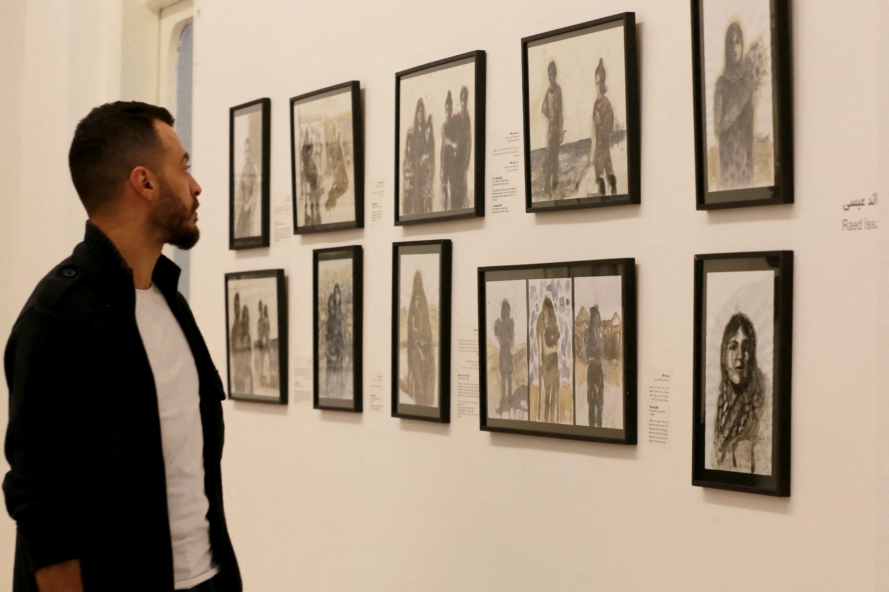Visitors look at drawings on the walls of Amman's Darat al-Funun gallery during a collective exhibition by four displaced Palestinian artists from Gaza, entitled "Under Fire", on November 5, 2024 (AFP)