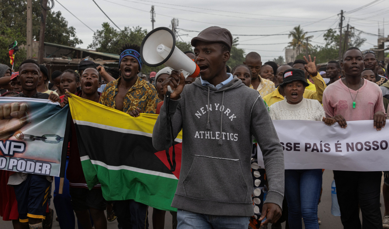 A protester speaks through a megaphone while protesting against the government, carrying the flag of Mozambique and the portrait of the presidential candidate of the Optimist Party for the Development of Mozambique (PODEMOS) Venancio Mondlane, in Maputo on November 6, 2024. (AFP)