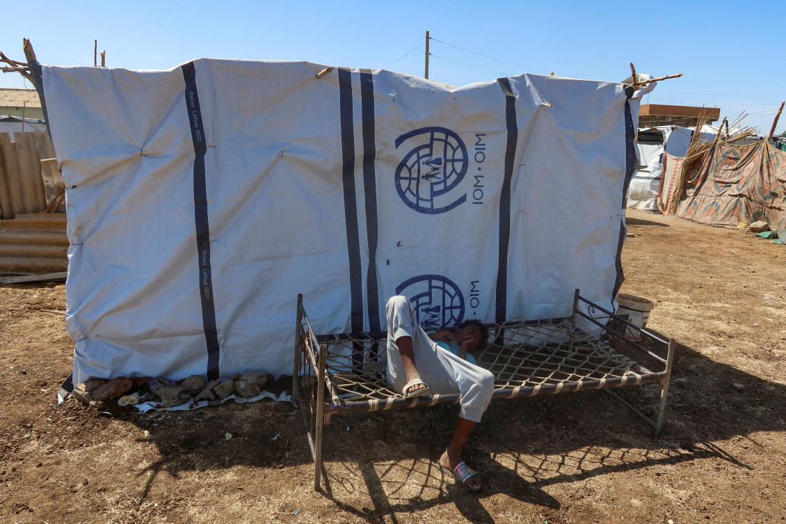 A boy displaced from Sudan's Gezira state due to Rapid Support Forces violence, lies down on a bench with the logo of the International Organization for Migration in New Halfa, Sudan, November 2, 2024. (Reuters)
