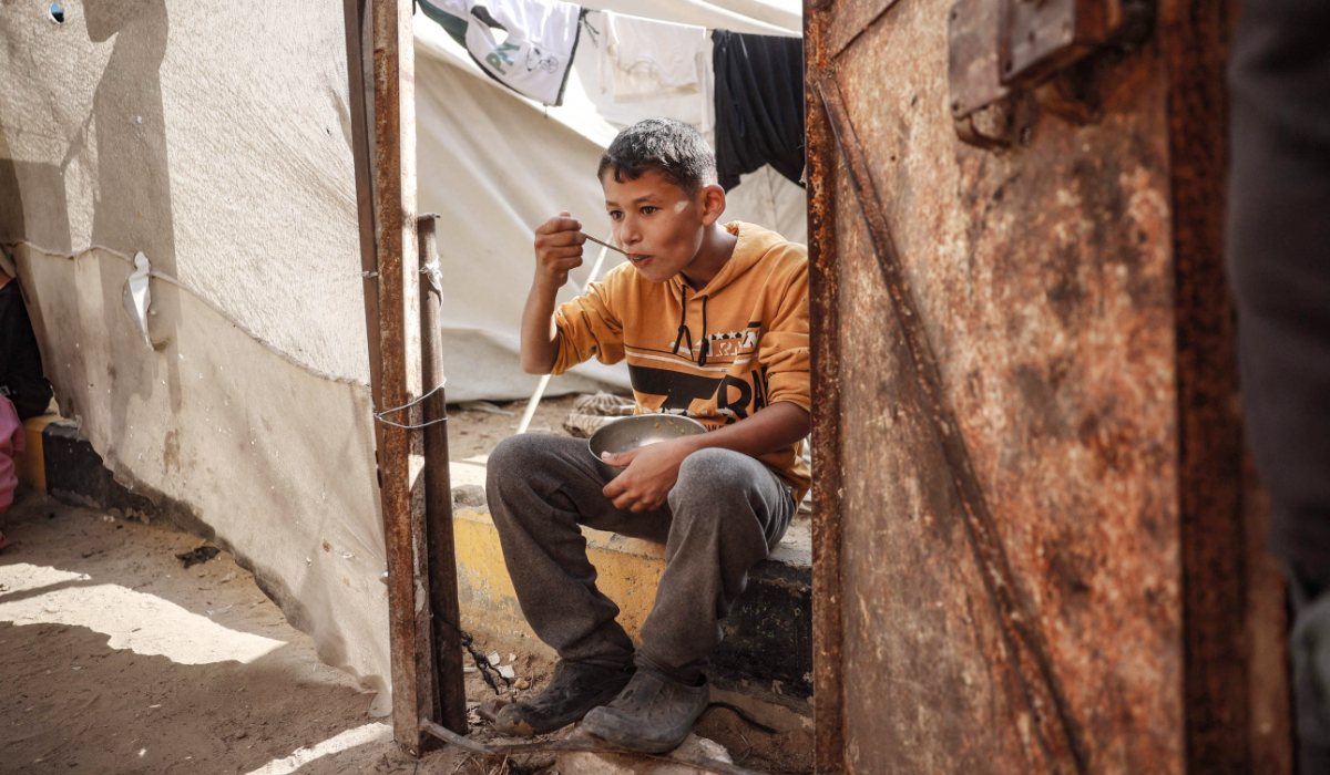 A displaced boy eats a hot meal that he received as aid from volunteers, at the Bureij refugee camp in Gaza. (AFP)