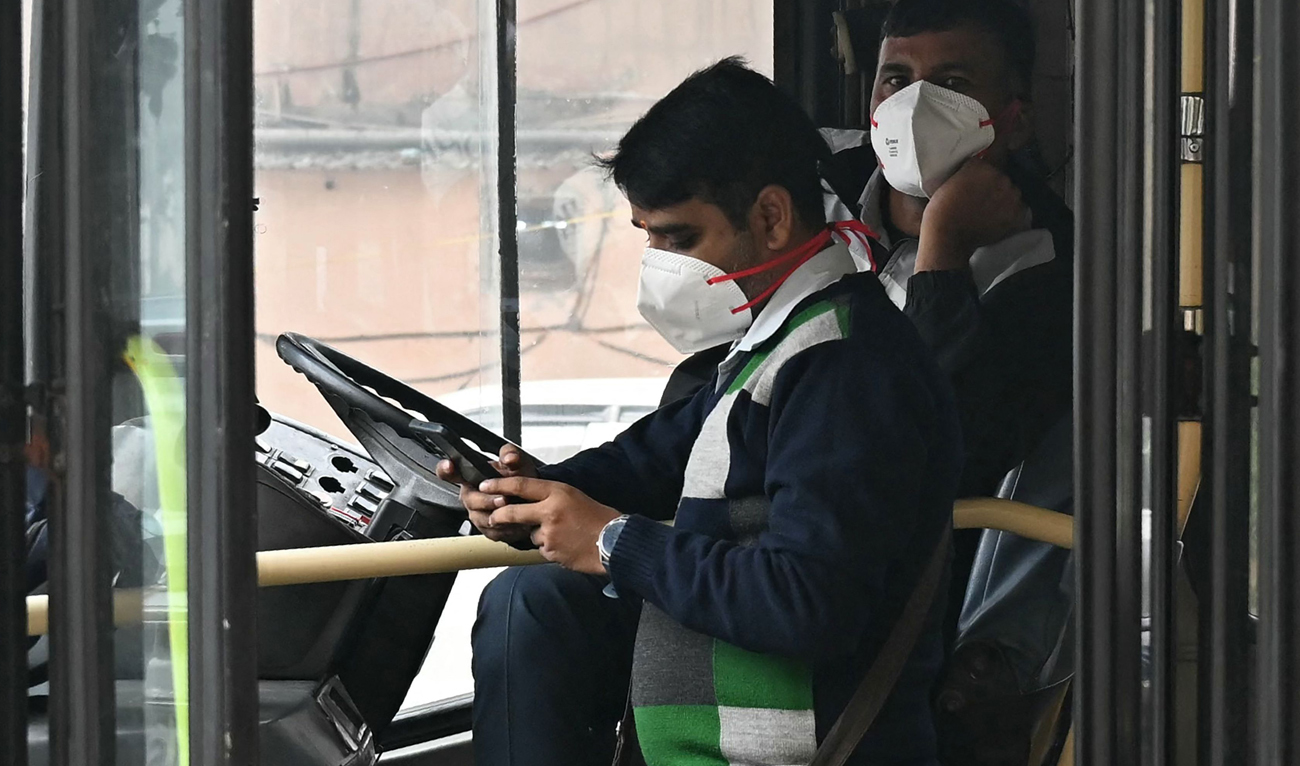 A bus driver and conductor wear masks amid smog, at a bus stop in New Delhi on November 18, 2024. (AFP)