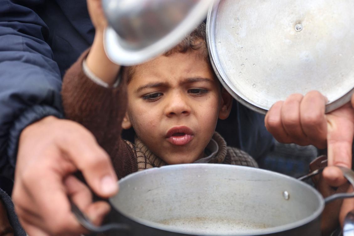 A Palestinian boy attempts to get a meal of lentils from a volunteer food distribution point, in Gaza City on November 19, 2024, as the war in the Palestinian territory between Israel and Hamas continues. (FilE/AFP)