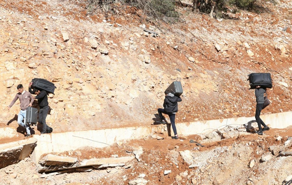 People fleeing Israeli bombardment in Lebanon cross a crater, caused by an Israeli strike, in the area of Masnaa on the Lebanese side of the border crossing with Syria, Nov. 20, 2024. (AFP)