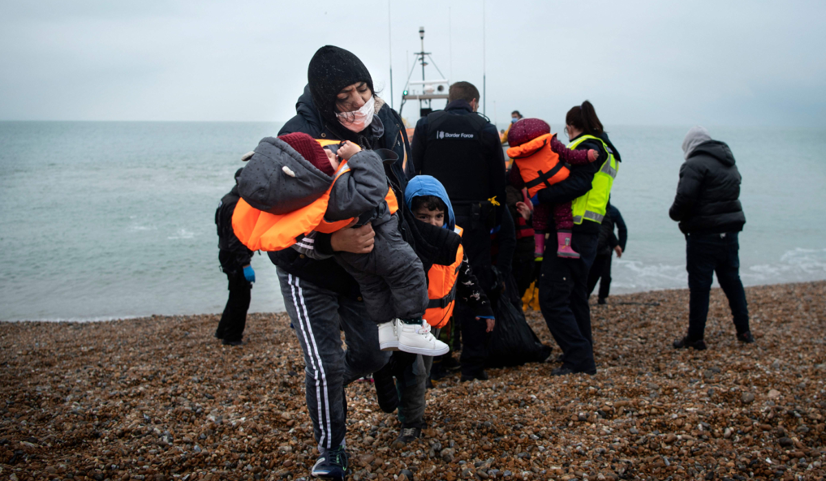 A migrant carries her children after being helped ashore from a RNLI (Royal National Lifeboat Institution) lifeboat at a beach in Dungeness, on the south-east coast of England, on November 24, 2021, after being rescued while crossing the English Channel. (AFP)