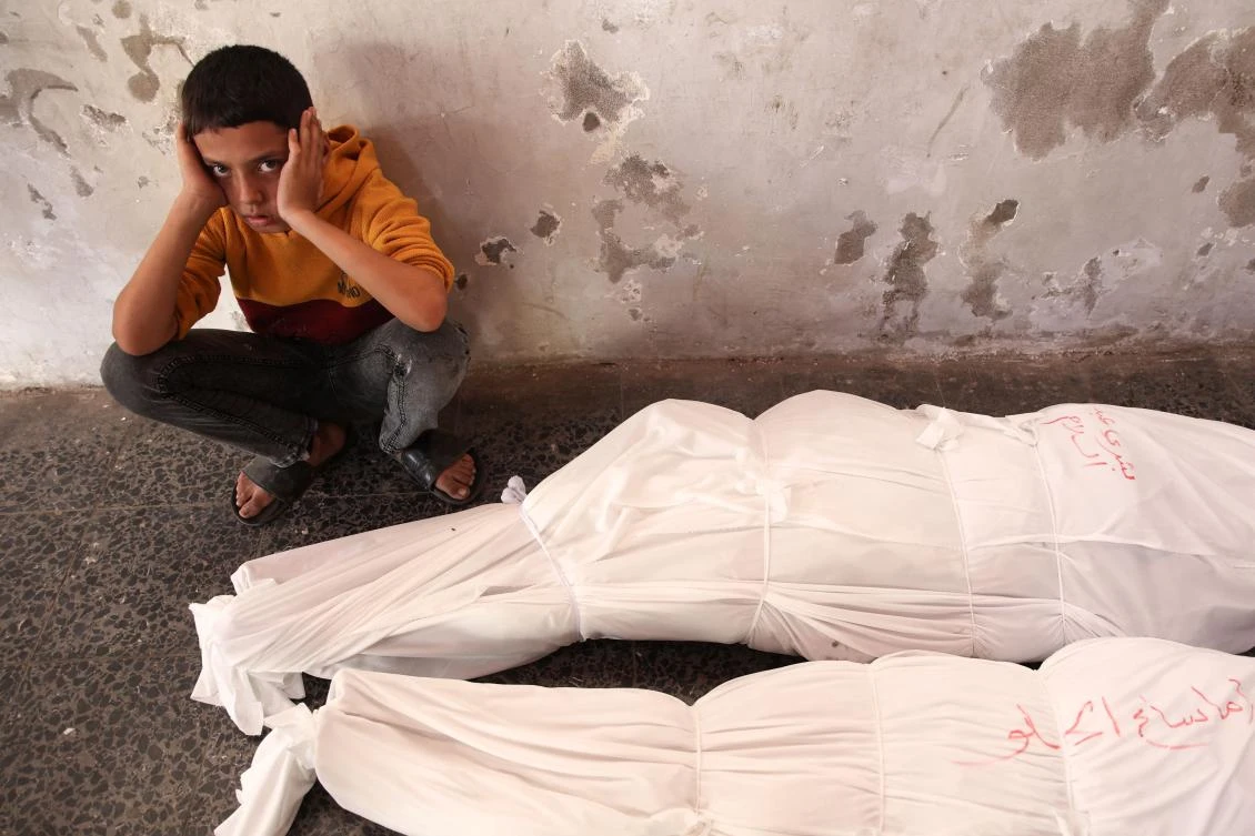 A Palestinian child sits next to the shrouded bodies of people killed in an Israeli strike. (AFP)