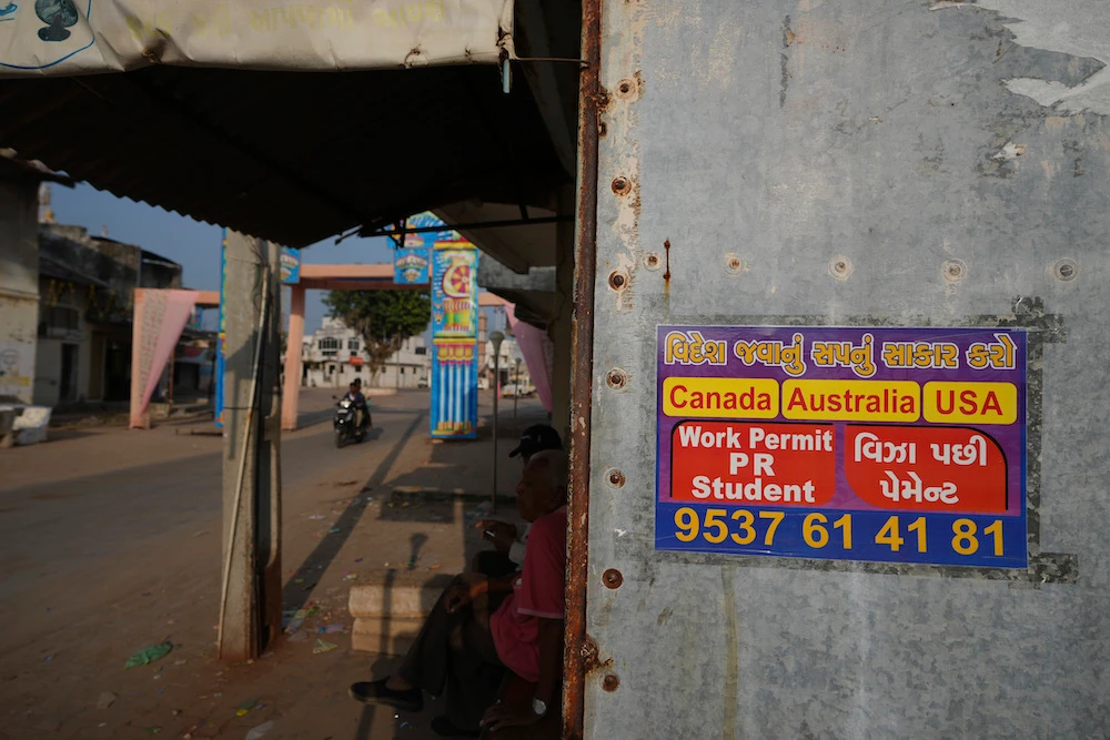 Above, an advertising poster pasted on a shop at Dingucha village in Gandhinagar, India where the family – who froze to death while being smuggled to the US – came from. (AP)